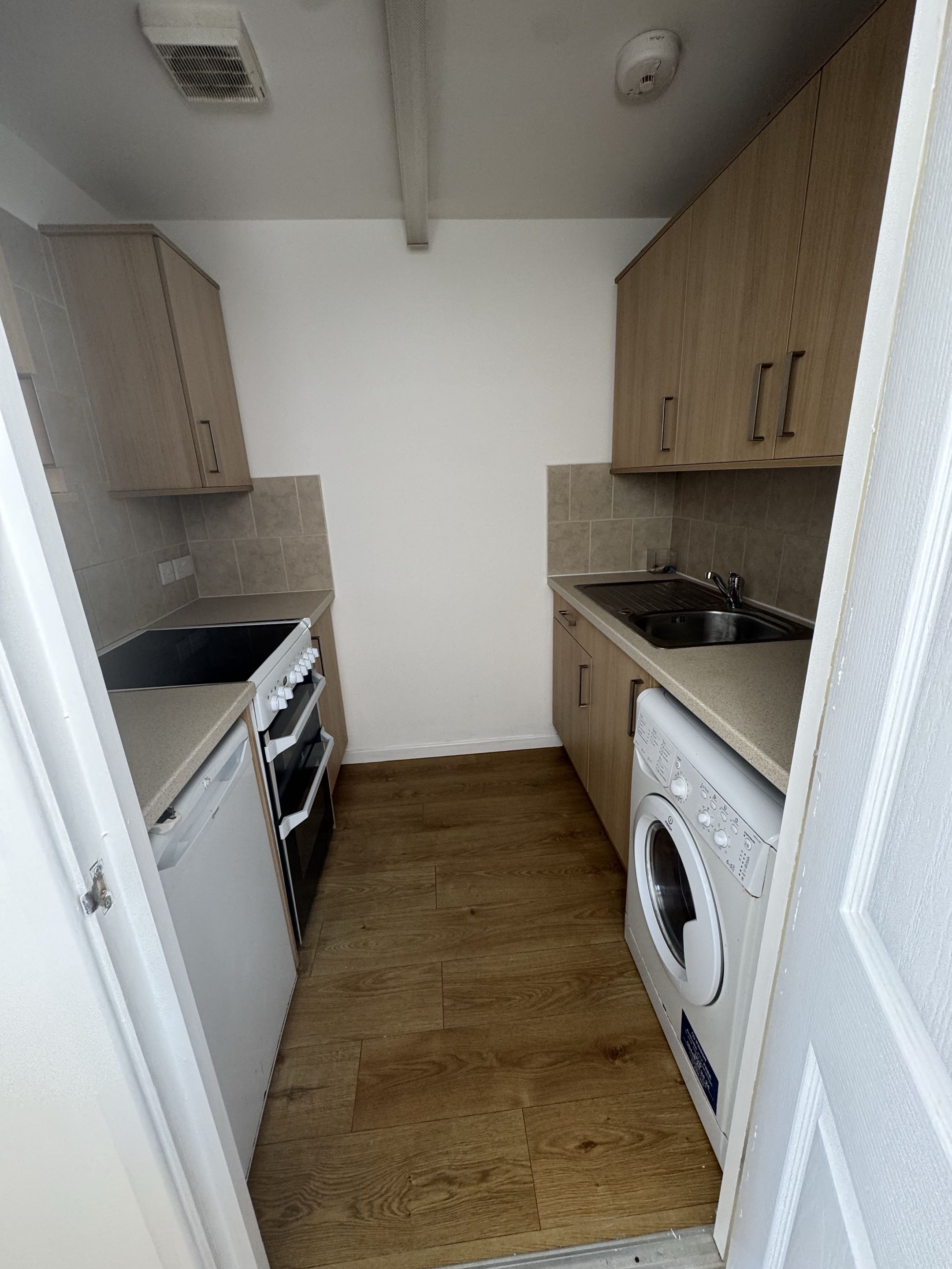 Freshly redecorated apartment kitchen with white walls and wood-effect flooring