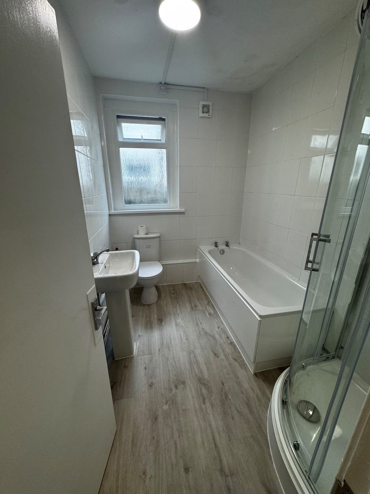 Renovated bathroom with wood-effect flooring, bath, basin and corner shower enclosure
