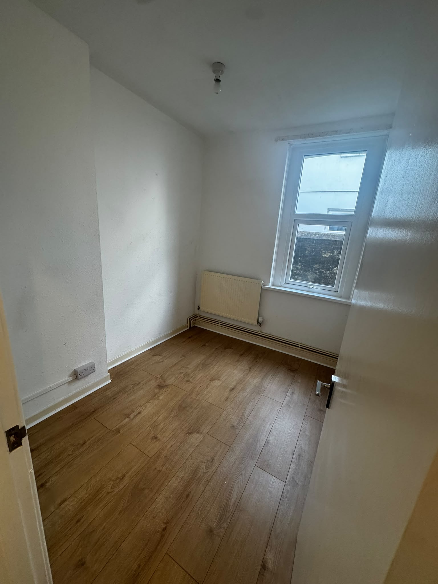 Small bedroom after renovation with new oak-effect flooring and clean walls