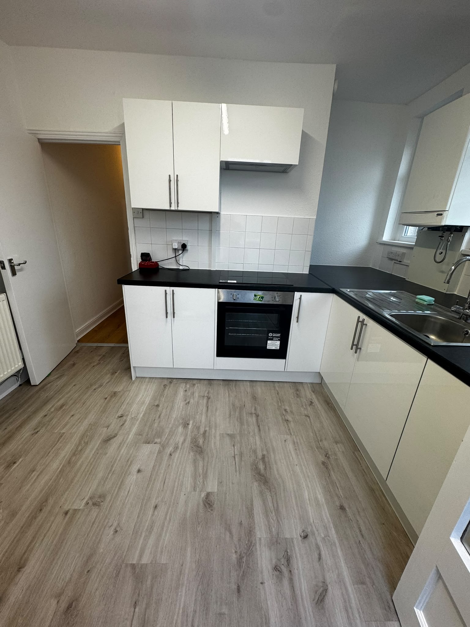 Renovated kitchen with gloss white units, black worktops, built-in oven and wood-effect flooring
