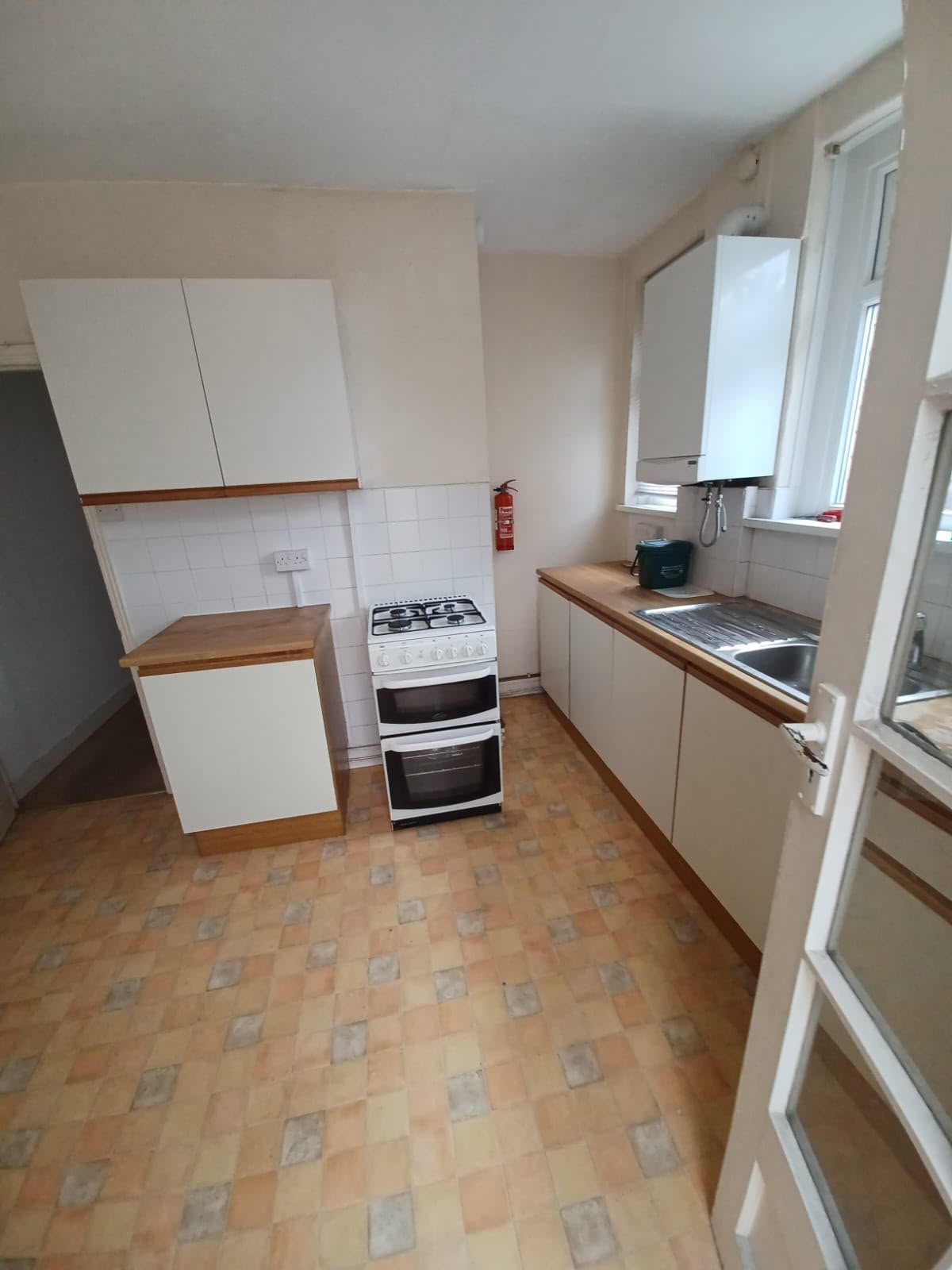 Dated kitchen with old wood-trim units and worn tiled vinyl floor before renovation